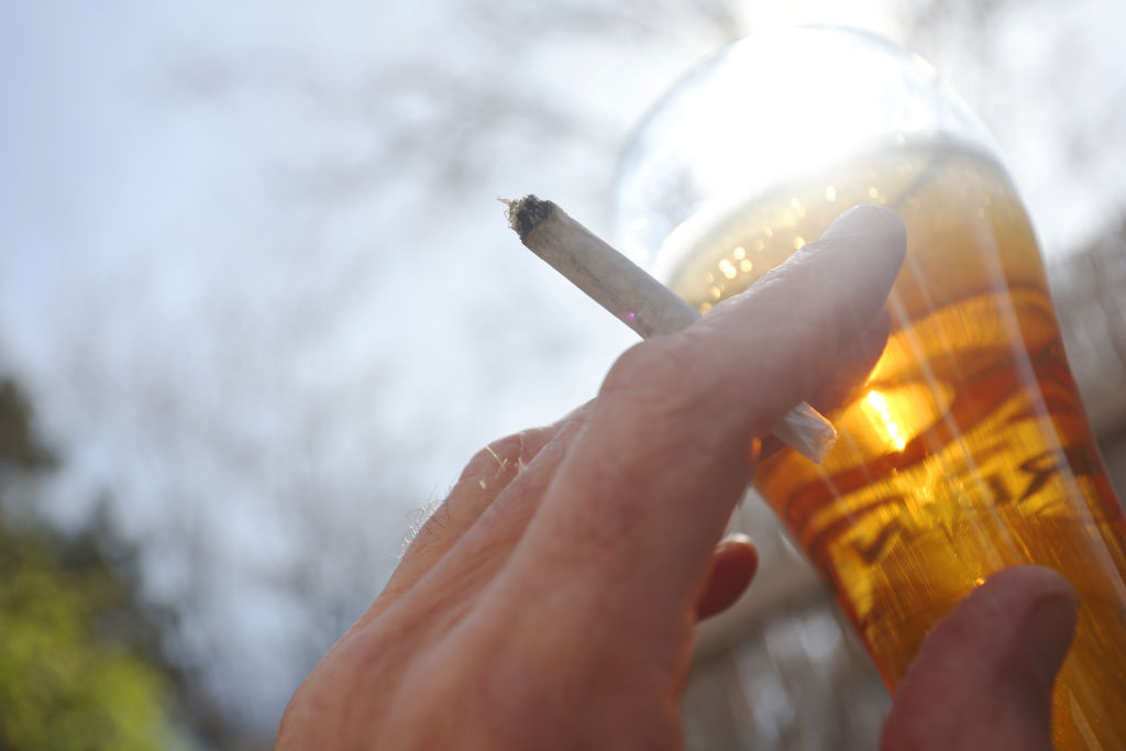 One hand holds a joint next to a glass of beer.